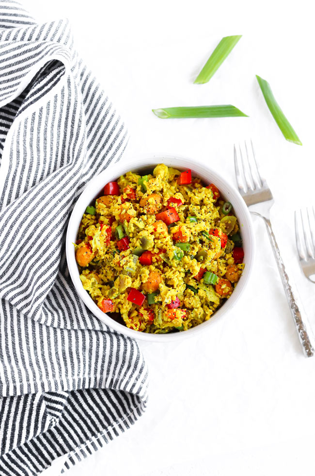 Cauliflower Turmeric Stir-Fry in a stoneware bowl next to a black and white striped towel and hammered silverware.