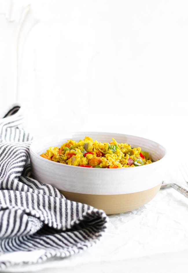Cauliflower Turmeric Stir-Fry in a stoneware bowl next to a black and white striped towel and hammered silverware.