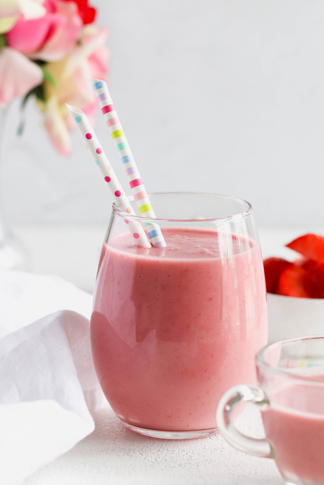 Dairy-Free Vanilla Strawberries and Cream Smoothie in a drinking glass with paper straws net to a floral bouquet and fresh strawberries.